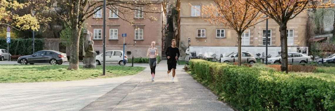 A couple jogging together in an urban park surrounded by greenery and houses.